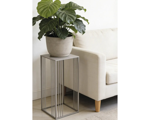 Modernt grått blomställ i metall med minimalistisk design, med en grön växt i kruka bredvid en ljus soffa i ett vardagsrum.