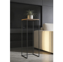 Modernt högt blomstativ med kvadratisk träskiva och svart metallstomme i ett ljust vardagsrum bredvid en soffa.