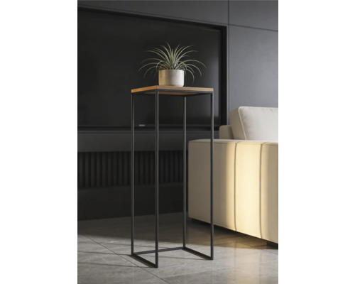 Modernt högt blomstativ med kvadratisk träskiva och svart metallstomme i ett ljust vardagsrum bredvid en soffa.