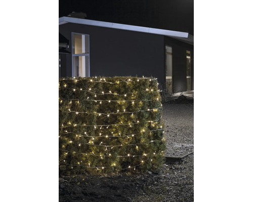 LED-ljusslinga för utomhusbruk i varmvitt, lindad runt en häck, nattetid framför ett modernt hus.