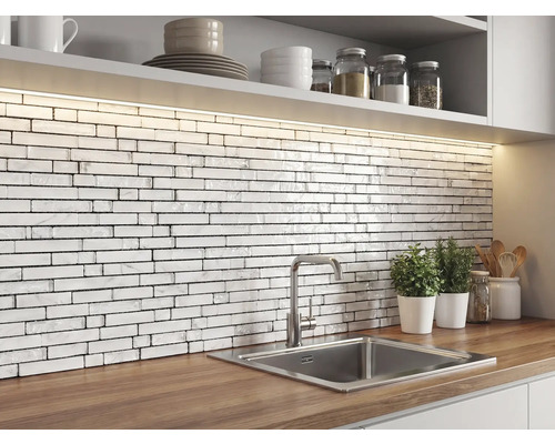 Kök med ett stänkskydd av vit mosaik i tegelstil med marmortextur, bänkskiva i trä, rostfri diskho och LED-belysning.