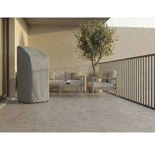 Ljus, modern terrass med ett grått skyddsöverdrag för trädgårdsutrustning, loungemöbler i metall och ett olivträd i kruka.