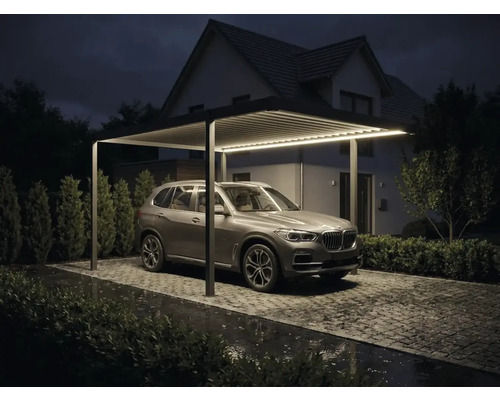 Modern carport i aluminium med integrerad led belysning, lamelltak och parkerad SUV på en stenlagd uppfart på natten.