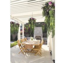 Matplats utomhus under en vit pergola med träbord, trästolar, hängande växter och en eldstad i sten på en stenlagd uteplats.