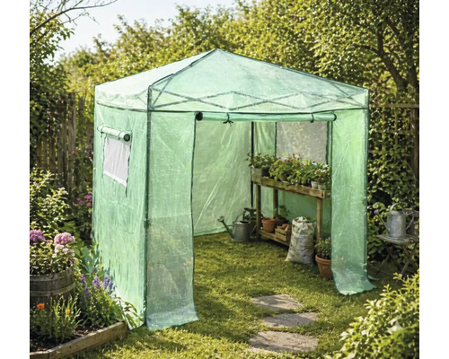 Växthustält av plastfolie i en trädgård med trähylla, växter i krukor, vattenkanna och jordsäck på gräsmattan.