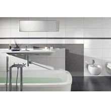 Modernt badrum med vitt badkar, vägghängt tvättställ och bidé, grå mosaik och stora vita väggplattor.