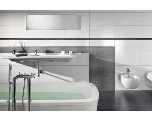 Modernt badrum med vitt badkar, vägghängt tvättställ och bidé, grå mosaik och stora vita väggplattor.