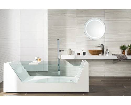 Modernt badrum med badkar i glas, fristående blandare, tvättställ i trä och belyst rund spegel.