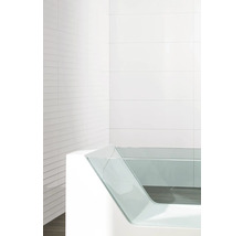 Modernt badkar med sidopanel i glas mot en vitkaklad bakgrund.