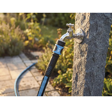 Textilslang med for_q Logo på en utomhuskran på en stenpelare i en trädgård.