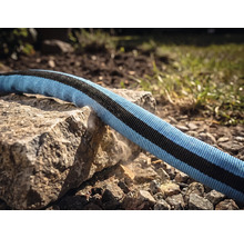 En textilträdgårdsslang dras över en vass stenkant för att demonstrera robusthet och slitstyrka.