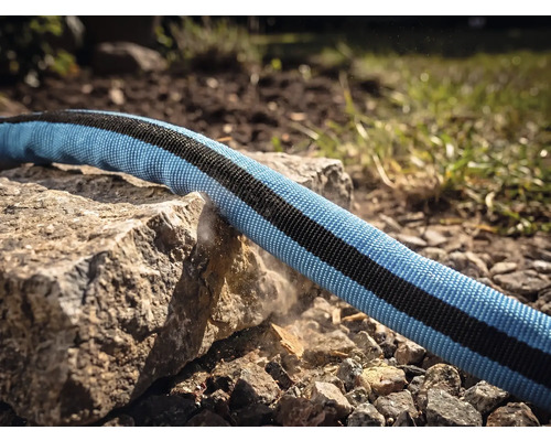 En textilträdgårdsslang dras över en vass stenkant för att demonstrera robusthet och slitstyrka.