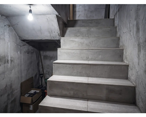 Betongtrappa i ett källarutrymme med oputsade väggar, upplyst av en glödlampa.