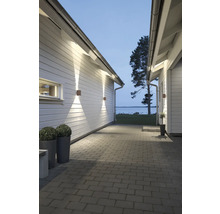 Stenlagd gång mellan vita trähus med moderna fyrkantiga utomhusvägglampor som lyser uppåt och nedåt. Utsikt över en sjö.