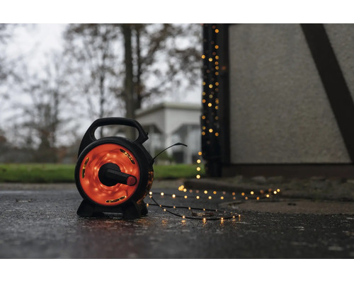 LED-ljusslinga på en svart rulle för utomhusbruk med varmvitt ljus på en våt mark bredvid en byggnad.