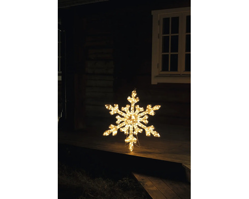Belyst LED-snöflinga med varmvitt ljus som juldekoration på en träterrass framför ett hus på natten.
