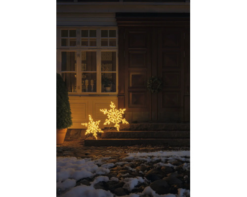 Två lysande LED-snöflingor i olika storlekar som juldekoration framför en husingång på trappsteg med varmvitt ljus.