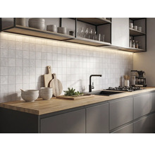 Modern köksmiljö med bänkskiva i trä, mörka skåp, kvadratiskt kakel, svart blandare och belysning under hyllorna.