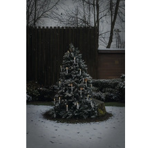 Snöig julgran utomhus med tända trådlösa LED ljus i en vinterträdgård.