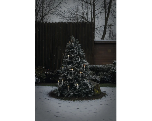 Snöig julgran utomhus med tända trådlösa LED ljus i en vinterträdgård.