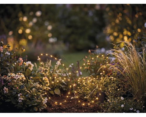 LED-trädgårdsdekoration i form av en fjäril med varmvita lampor i en blomrabatt.
