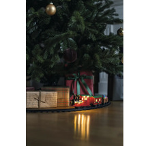Jultåg på räls under en dekorerad julgran med julklappar på ett trägolv.