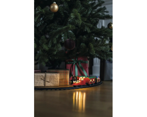 Jultåg på räls under en dekorerad julgran med julklappar på ett trägolv.