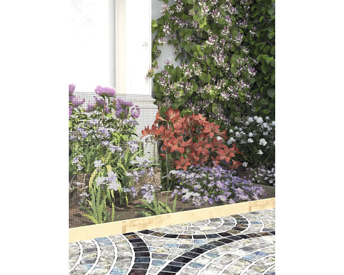 Trädgårdsrabatt med blommor skyddad av ett finmaskigt svart skyddsnät över en ljus träkant vid en stenlagd gång.