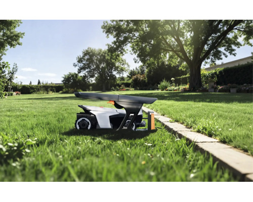 Robotgräsklippare under ett skyddstak på en gräsmatta i en solig trädgård med träd och stenkant.