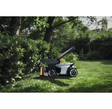 Robotgräsklippare med tillbehör på en gräsmatta i trädgården bredvid en häck.