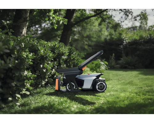Robotgräsklippare med tillbehör på en gräsmatta i trädgården bredvid en häck.
