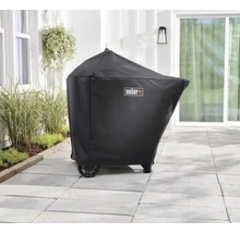 Svart grillöverdrag med Weber Logo på en ljus stenterrass utomhus bredvid växter.