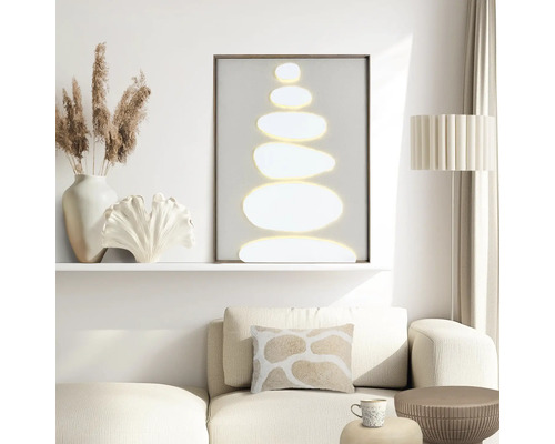 Modern vardagsrum med en minimalistisk tavla med staplade stenar, en beige soffa med en mönstrad kudde och dekorativa tillbehör.