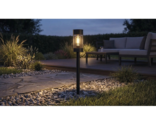 Solcellsdriven trädgårdsbelysning med LED-lampa och nätmönster som belyser en trädgårdsgång på natten bredvid en loungegrupp.