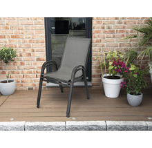 Stapelbar trädgårdsstol med aluminiumram och textilsits på en terrass med trädäck och växter framför en tegelvägg.
