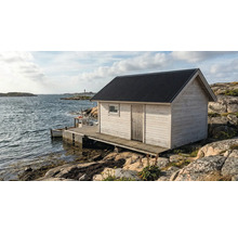 Trädgårdsstuga i vitt trä med mörkt korrugerat tak på en träbrygga vid havet på en klippig kust.