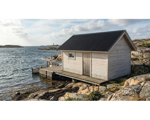 Trädgårdsstuga i vitt trä med mörkt korrugerat tak på en träbrygga vid havet på en klippig kust.