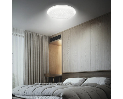Modern LED-taklampa med stjärnhimmelseffekt i ett ljust sovrum med trävägg och grå textilier.