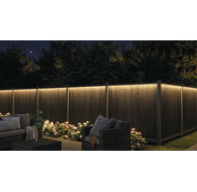 Belyst trädgårdsstaket med LED-list på natten, trädgårdsmöbler och blommor.