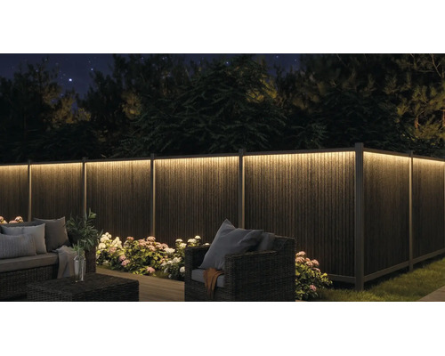 Belyst trädgårdsstaket med LED-list på natten, trädgårdsmöbler och blommor.