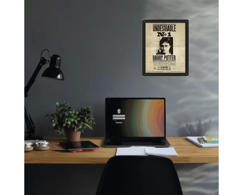 Inramad Harry Potter-poster Undesirable nummer 1 på en grå vägg ovanför ett organiserat skrivbord i trä med bärbar dator och lampa.