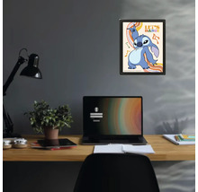Inramad poster med Disney-karaktären Stitch och texten Let's Dance ovanför ett skrivbord med laptop och lampa i ett modernt arbetsrum.