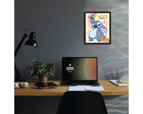 Inramad poster med Disney-karaktären Stitch och texten Let's Dance ovanför ett skrivbord med laptop och lampa i ett modernt arbetsrum.