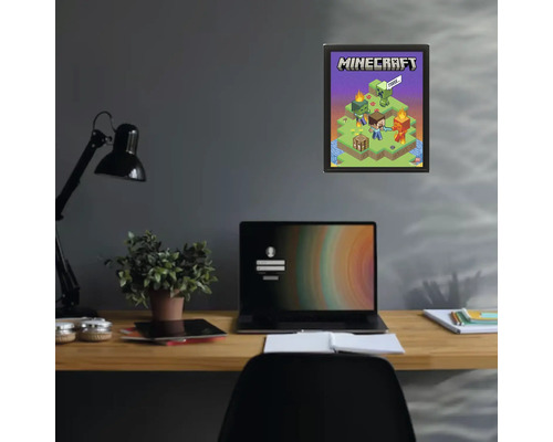 Minecraft-poster i en svart ram på en mörk vägg ovanför ett skrivbord med en bärbar dator och en växt.