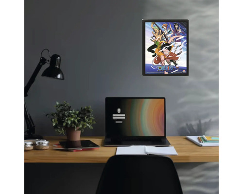 Inramad One Piece-poster på en vägg ovanför ett skrivbord med bärbar dator och krukväxt.