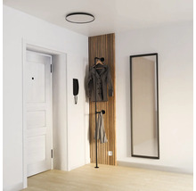 Ljus, modern hall med en vertikal akustikpanel av trälaminat, en svart klädhängare, en stor väggspegel och en vit dörr.