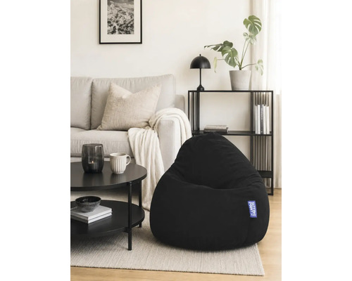 Svart saccosäck i ett ljust, modernt vardagsrum med grå soffa, svart soffbord och hylla.