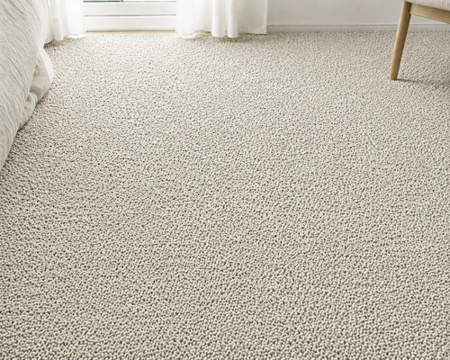 Strukturerad heltäckningsmatta i bouclé-stil i ett ljust rum med säng, gardin och stolsben.