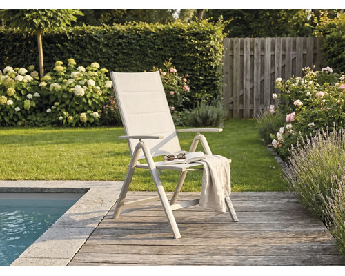 Modern hopfällbar trädgårdsstol med högt ryggstöd på en träaltan vid en pool, omgiven av en grönskande trädgård med blommor.