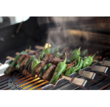 Kött och grön paprika på metallspett över ett varmt grillgaller med stigande ånga.